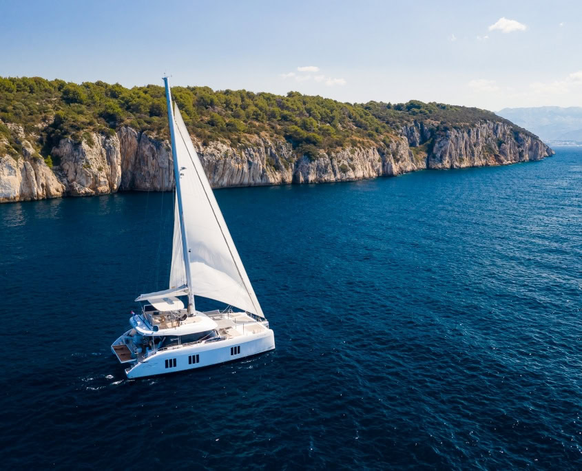 Elegant sailing yacht cruising along scenic coastline with cliffs and lush greenery.