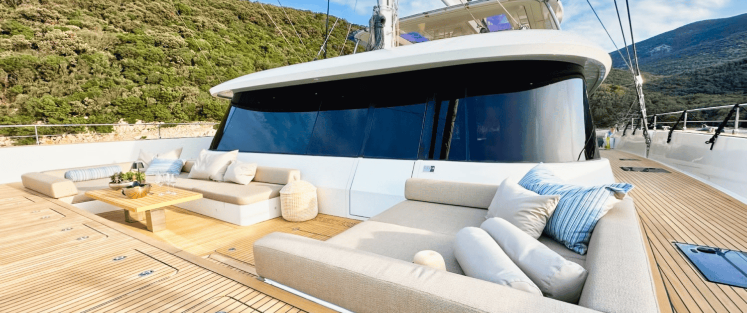 Sunreef 80 yacht deck with outdoor lounge and scenic mountain backdrop.
